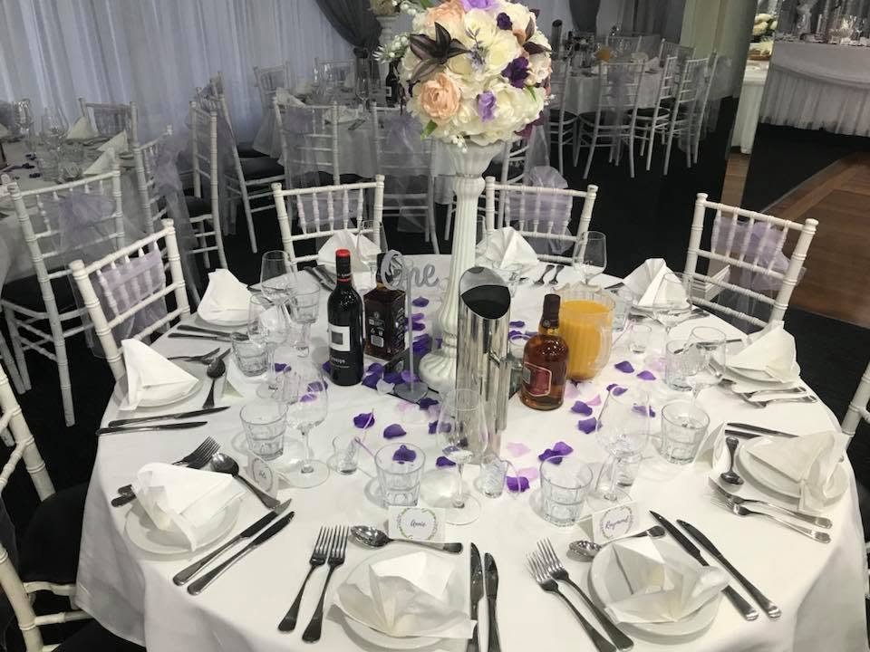 Exquisite indoor reception dining table with white chairs, centerpieces, and place settings