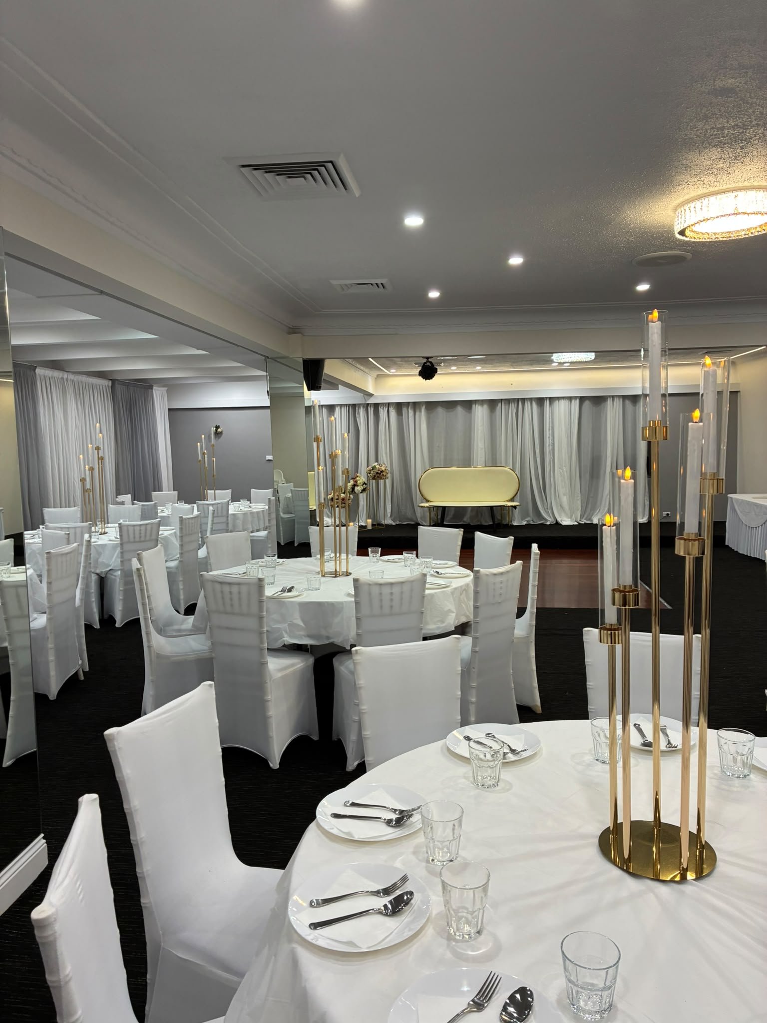 Spacious grand reception ballroom with round banquet tables, glowing candelabras, and elevated stage